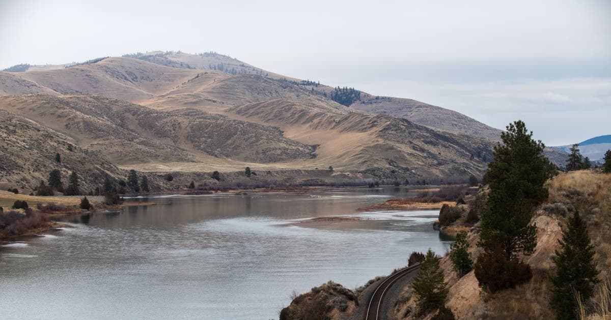Peaceful river with mountains and railway in Montana's natural landscape.