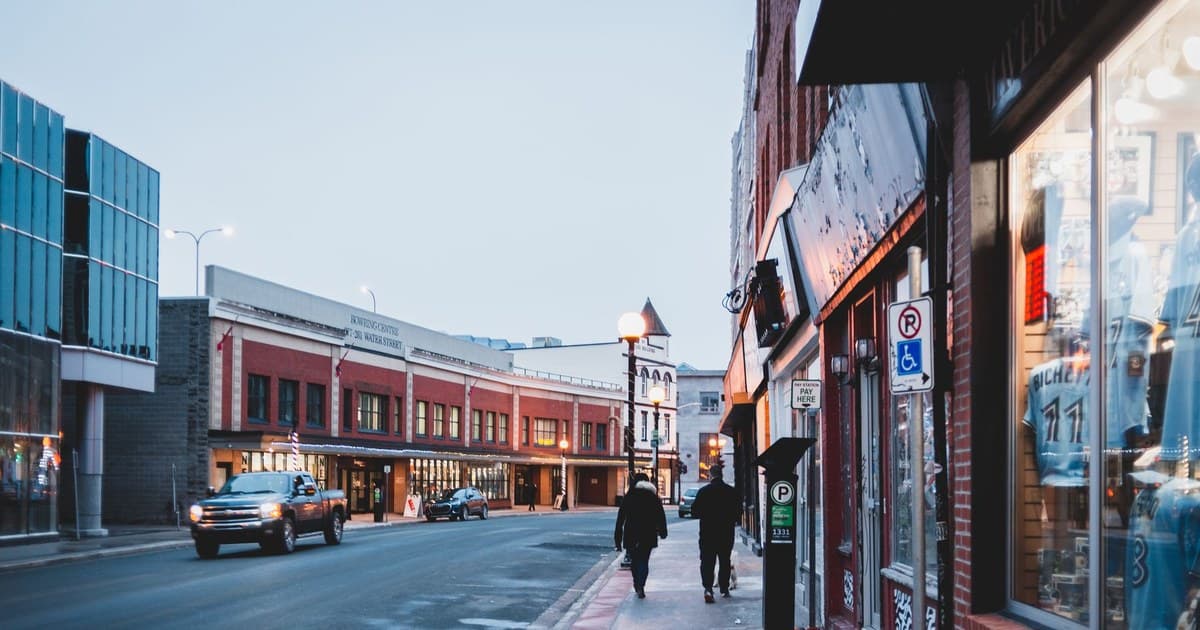 A lively urban street with storefronts, pedestrians, and vehicles during the day, evoking a bustling atmosphere.