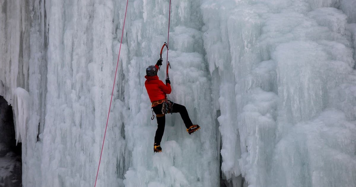 A climber in red jacket ascends a massive frozen waterfall, showcasing their ice climbing skills.